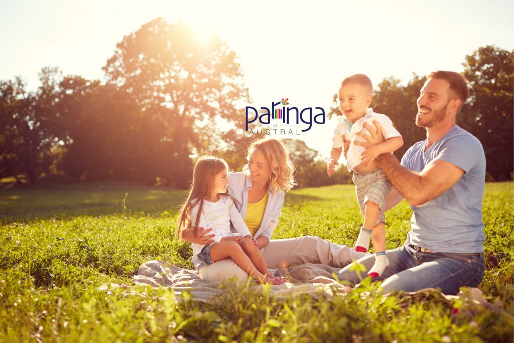A family sitting together on the grass in evening sunlight, with the Paringa at Austral logo